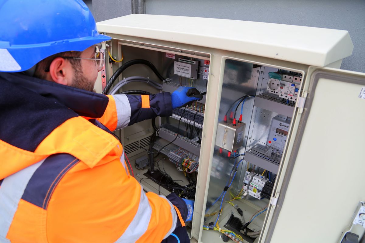 Electrician in hard hat and hi-vis working inside an electrical panel