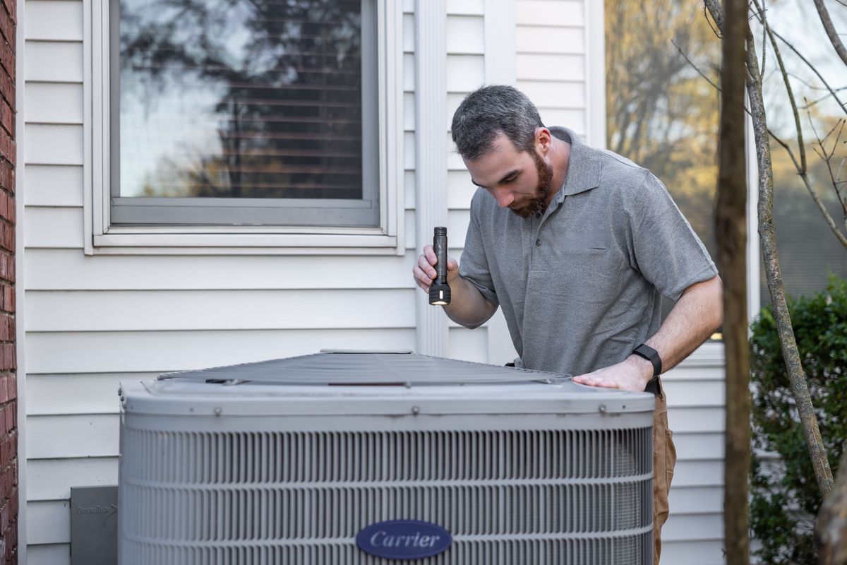 Technician inspecting an outdoor air conditioning condenser unit at a home